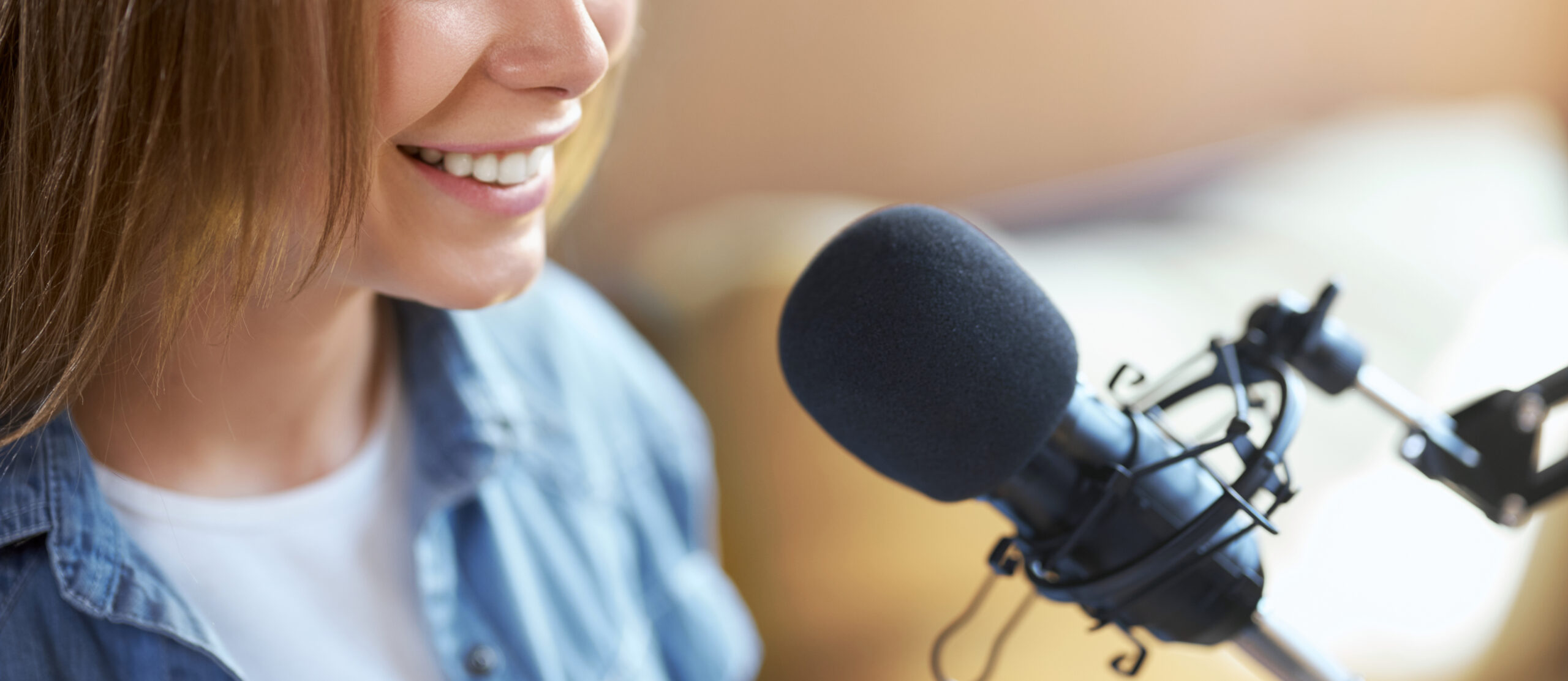 Close up of attractive young woman with good mood communicating in modern microphone with people online. Concept of process talking or recording interesting information.